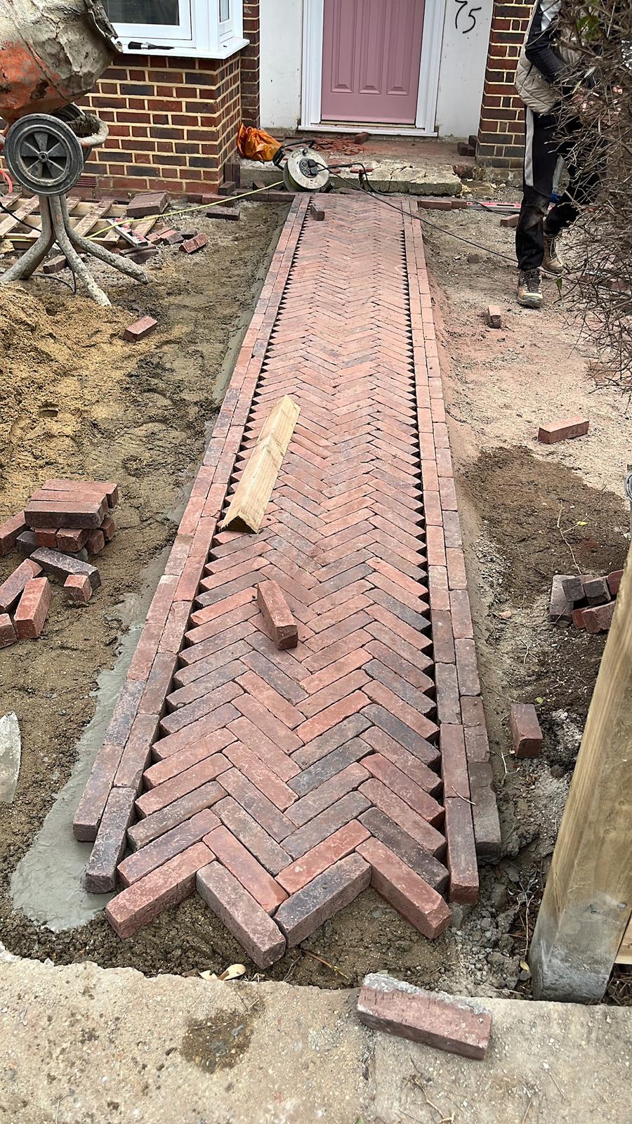 Herringbone brick path partly laid with loose bricks and edging