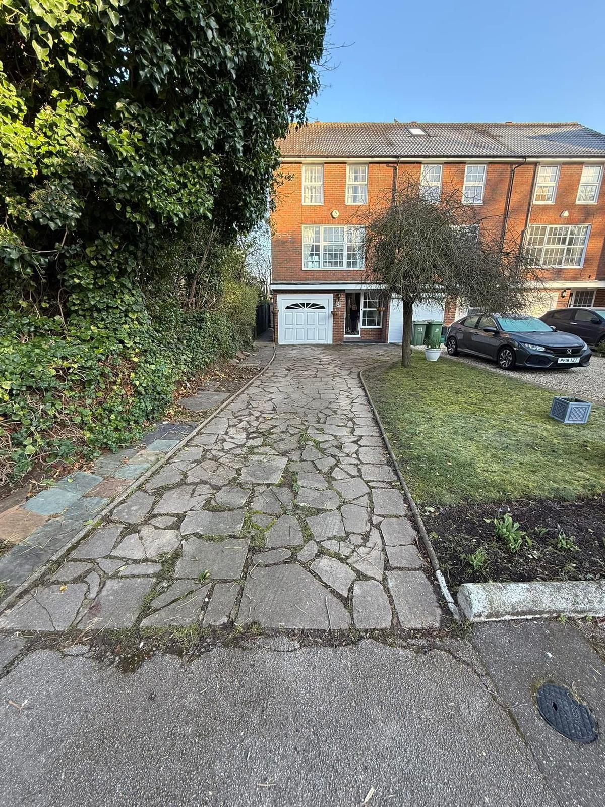 Old cracked crazy-paving driveway leading to a white garage before resin installation